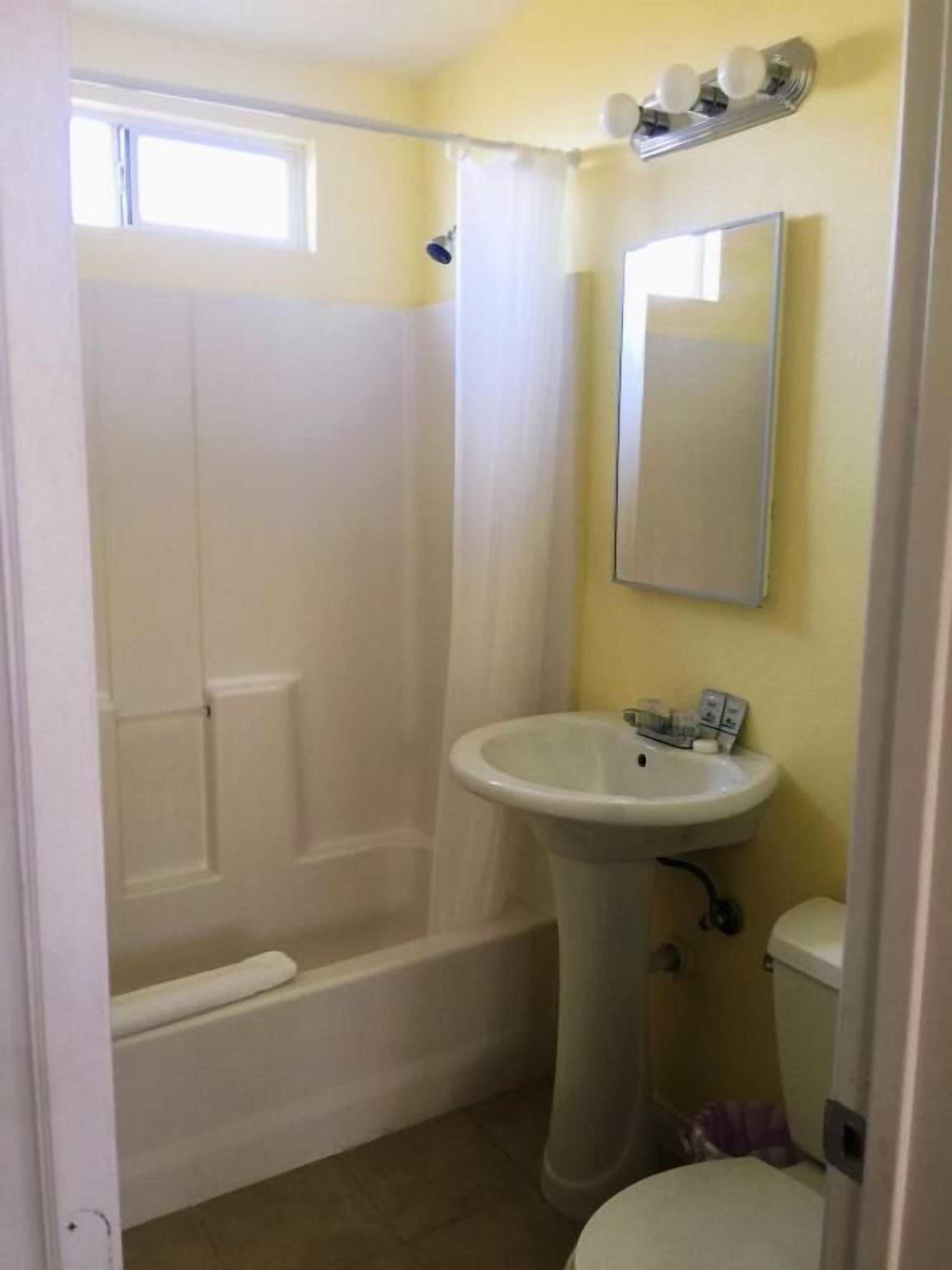 Et badeværelse med badekar, et håndvaskstel, toilet og et vindue med gardin.