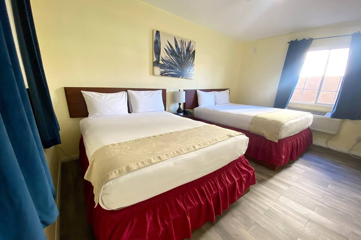 Habitación de hotel con dos camas, un cuadro grande en la pared y una ventana con cortinas.