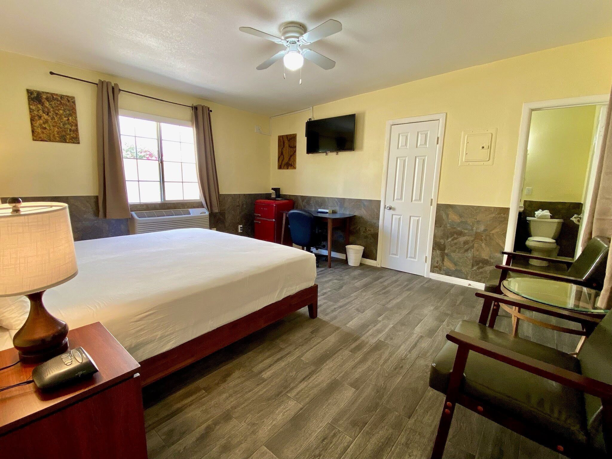 A hotel room with a bed, a desk, a chair, a TV, and a ceiling fan.