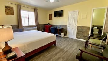 A hotel room with a bed, a desk, a chair, a TV, and a ceiling fan.