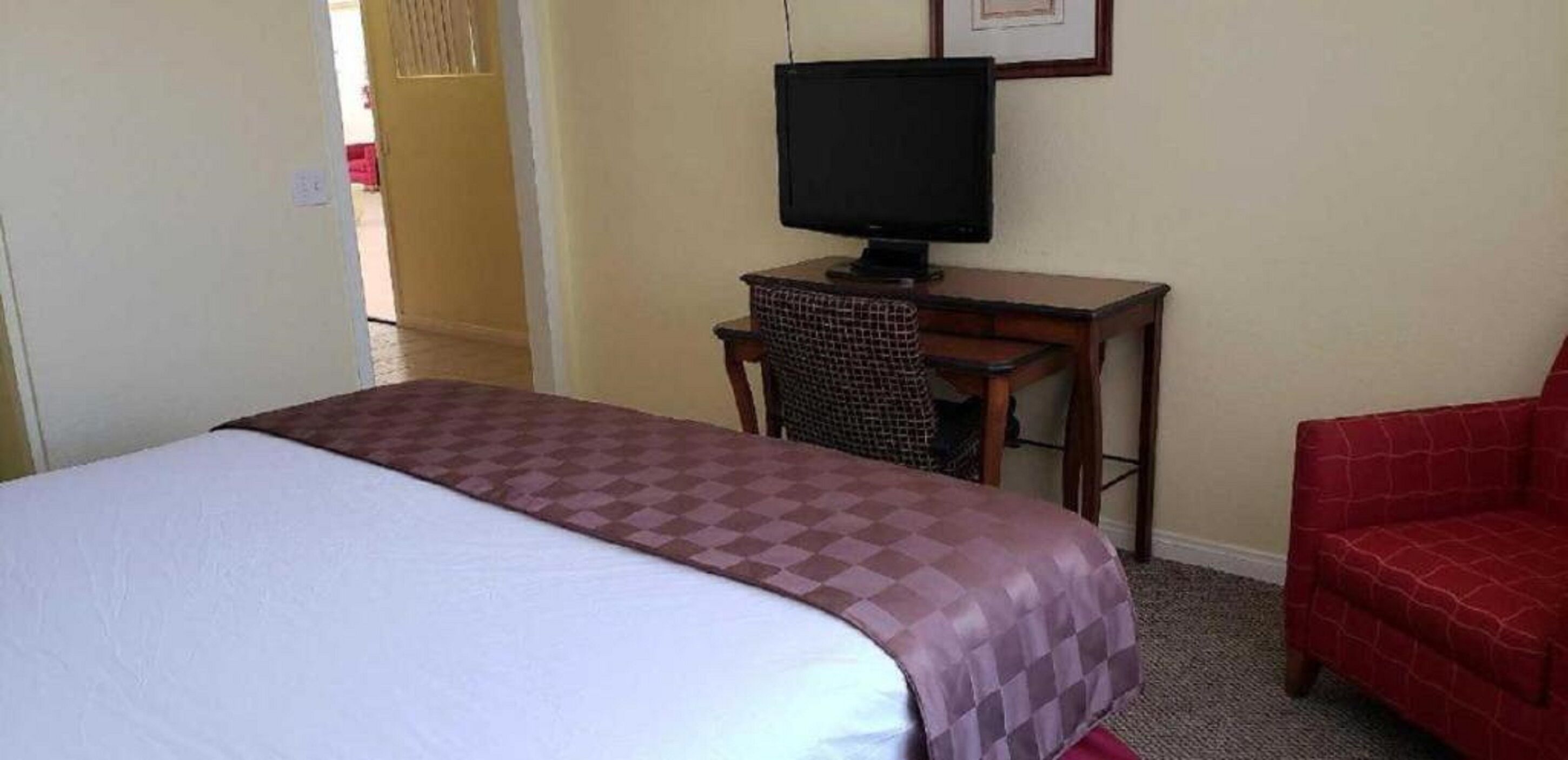 A hotel room with a bed, a desk with a television, and a red chair.