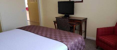 A hotel room with a bed, a desk with a television, and a red chair.