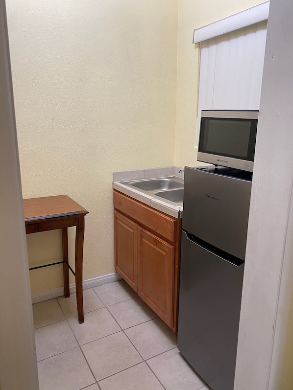 Una cocina compacta con microondas integrado, refrigerador de acero inoxidable y alacenas de madera.