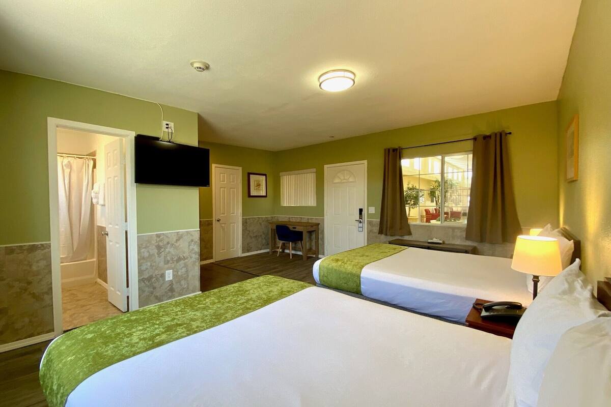 Habitación de hotel con dos camas, un escritorio, una silla, un televisor y una ventana con cortinas.