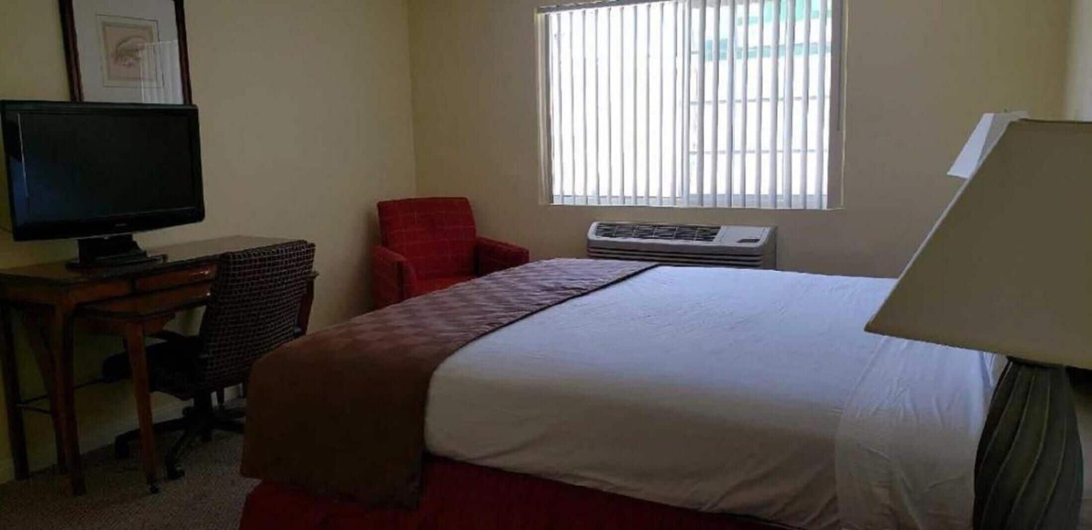 Une chambre d’hôtel équipée d’un lit, d’un bureau avec une télévision, d’une chaise et d’un appareil de climatisation.