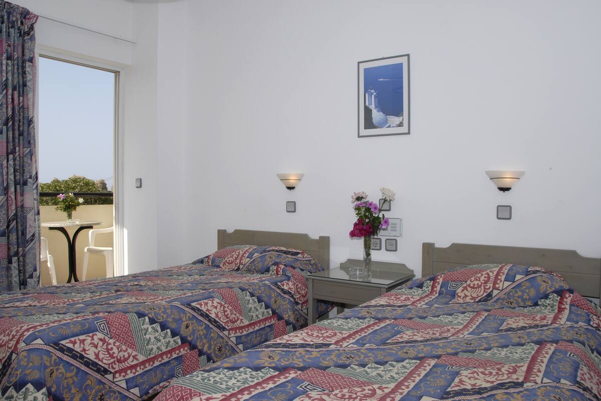A hotel room with two beds, a small table, a vase with flowers, and a framed picture on the wall.