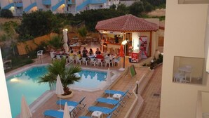 A pool area with lounge chairs and umbrellas, a small bar, and a dining area with people. - Sunshine Garden (Hersonissos)