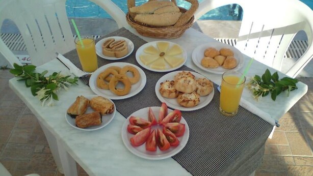 A dining table with various breakfast items and a basket of bread by a poolside chair. - Sunshine Garden (Hersonissos)
