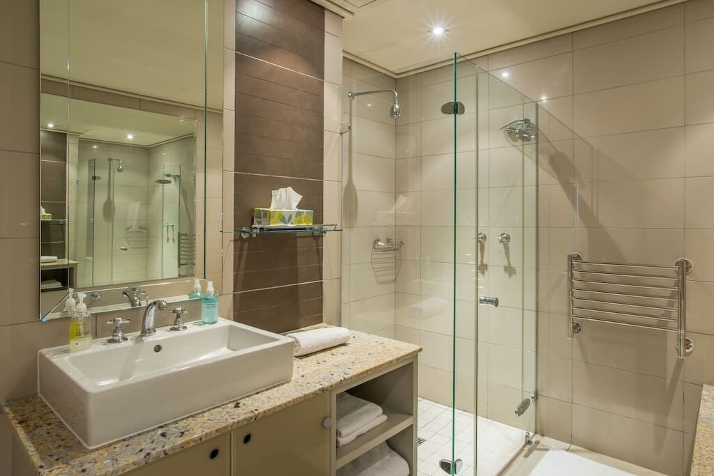 A modern bathroom with a glass-enclosed shower, a sink with a marble countertop, and a mirror above the sink.