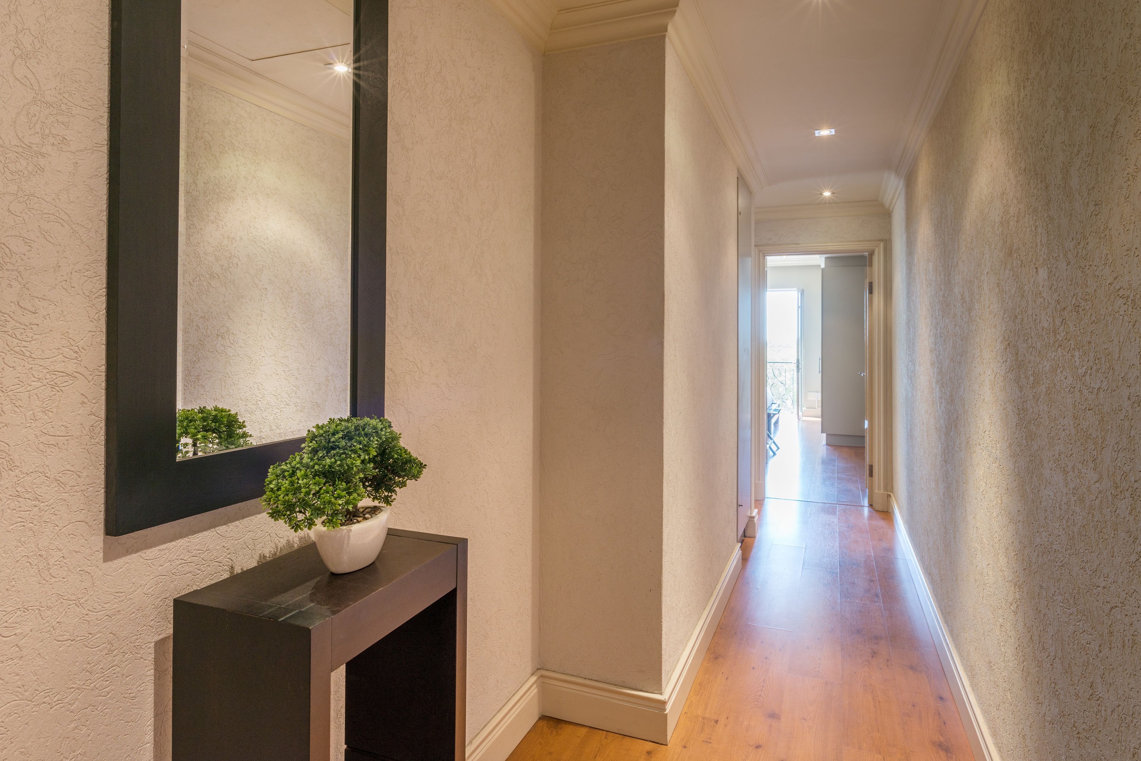 Un couloir avec une plante en pot posée sur une console, un grand miroir et un plancher en bois.
