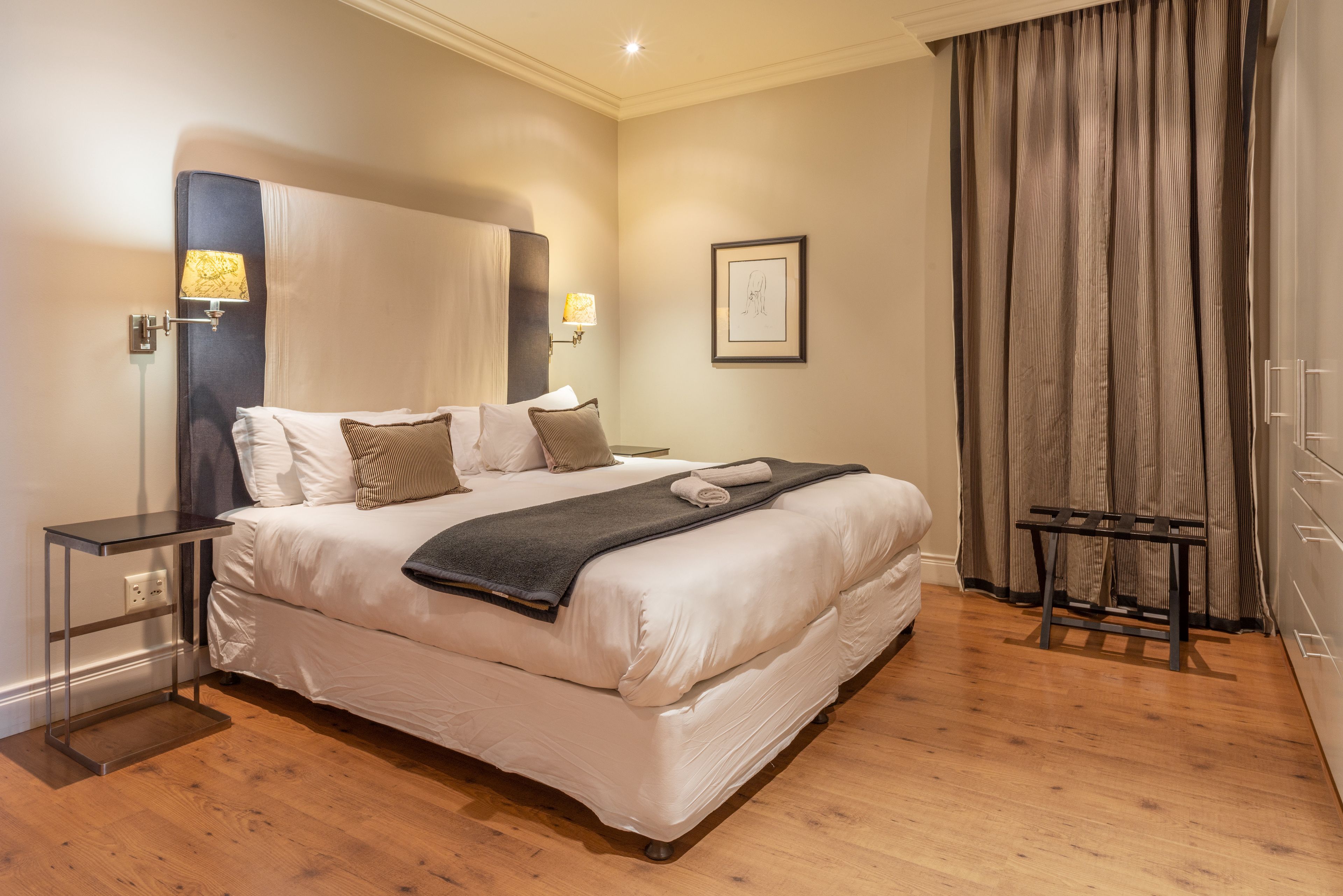 A neatly made bed with a headboard, bedside lamps, and a framed picture on the wall.