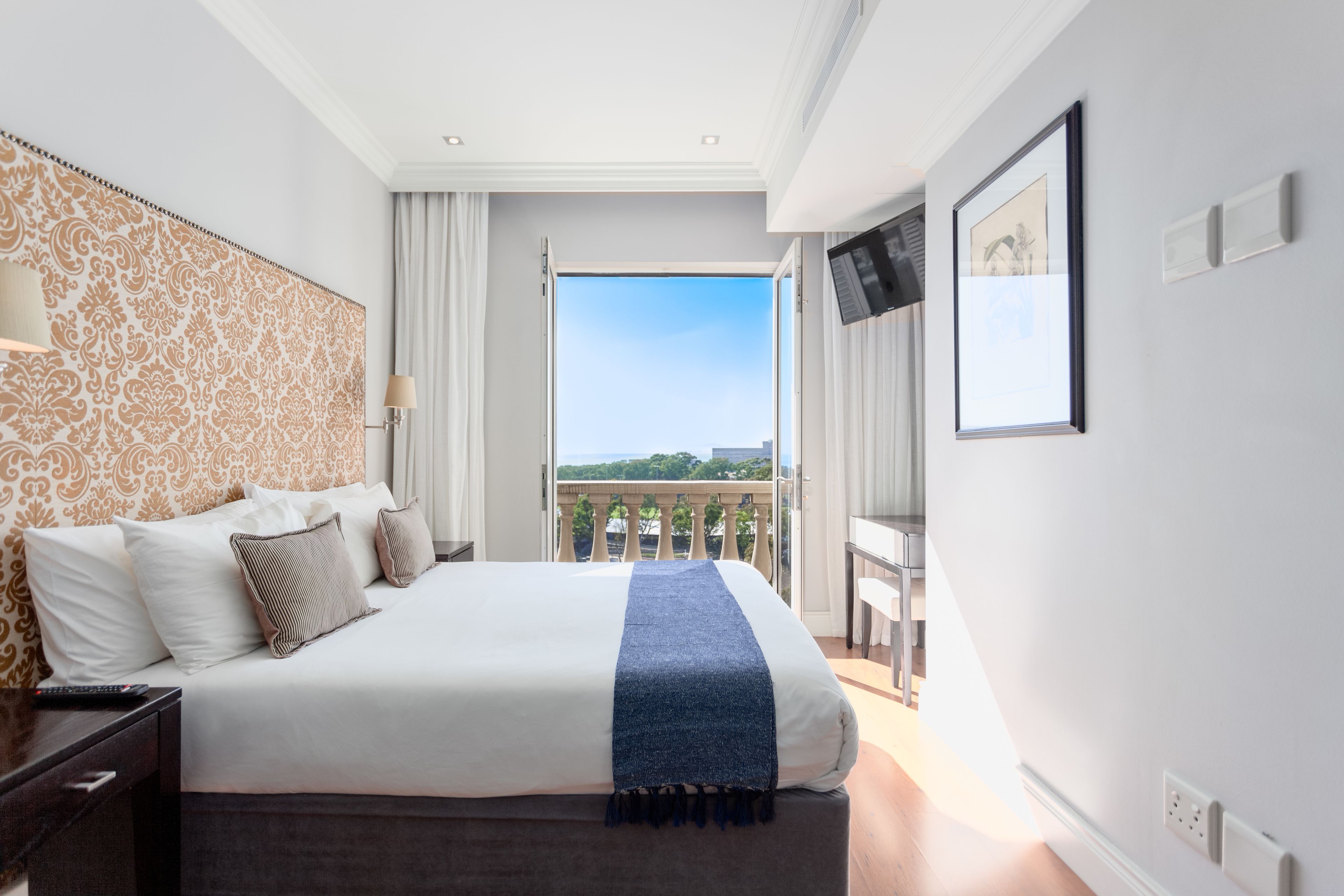 A hotel room with a large bed, a balcony with a view, and a television on the wall.