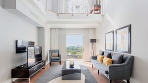 A modern living room with a flat-screen TV, a sofa, a coffee table, and a balcony with a view.