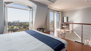 A bedroom with a large bed, a view of the city, and a balcony with a railing.