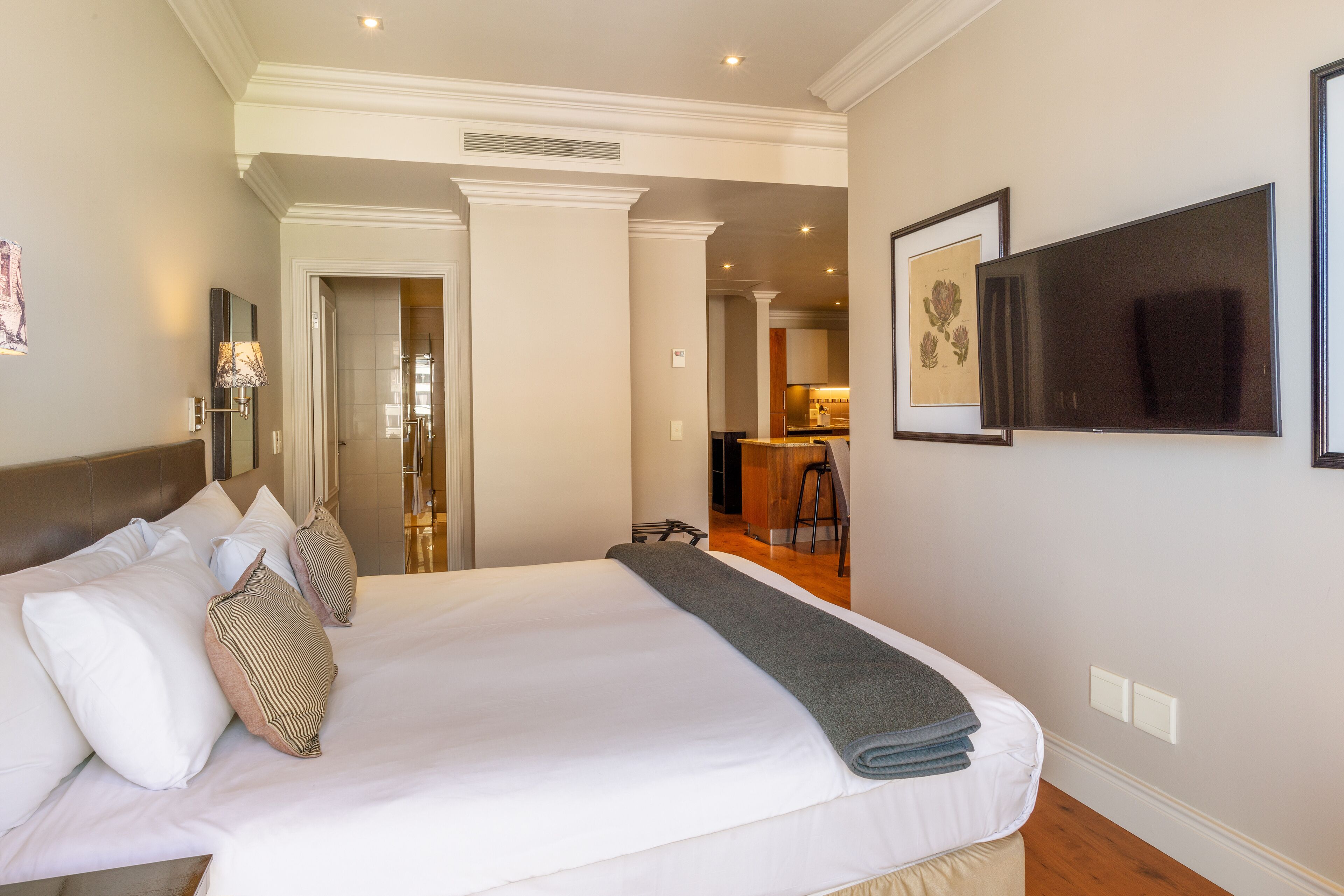 A hotel room with a large bed, a flat-screen TV, and a view into the kitchen area.
