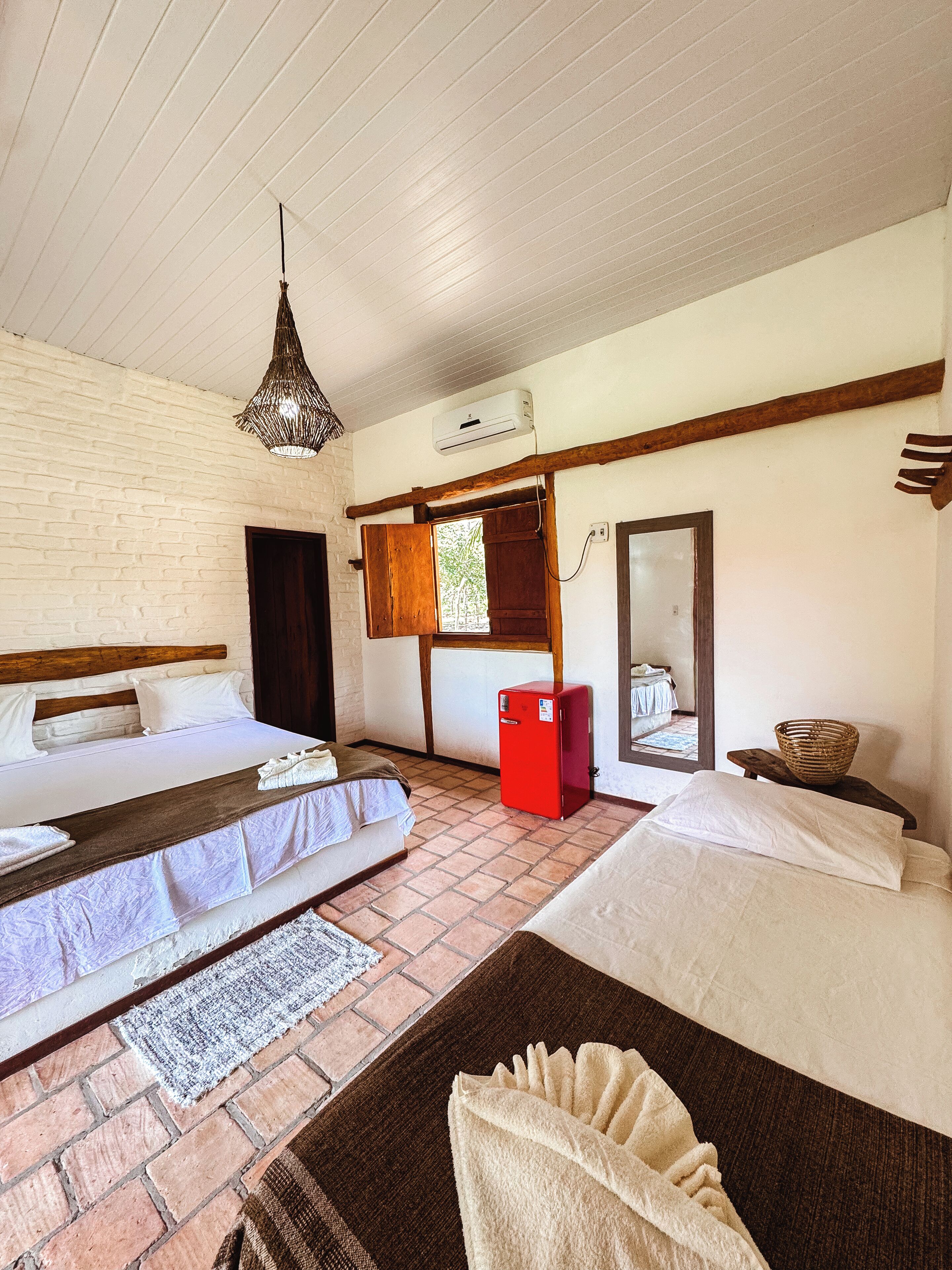 Une chambre avec deux lits, un réfrigérateur rouge, un panier en osier et un luminaire suspendu.