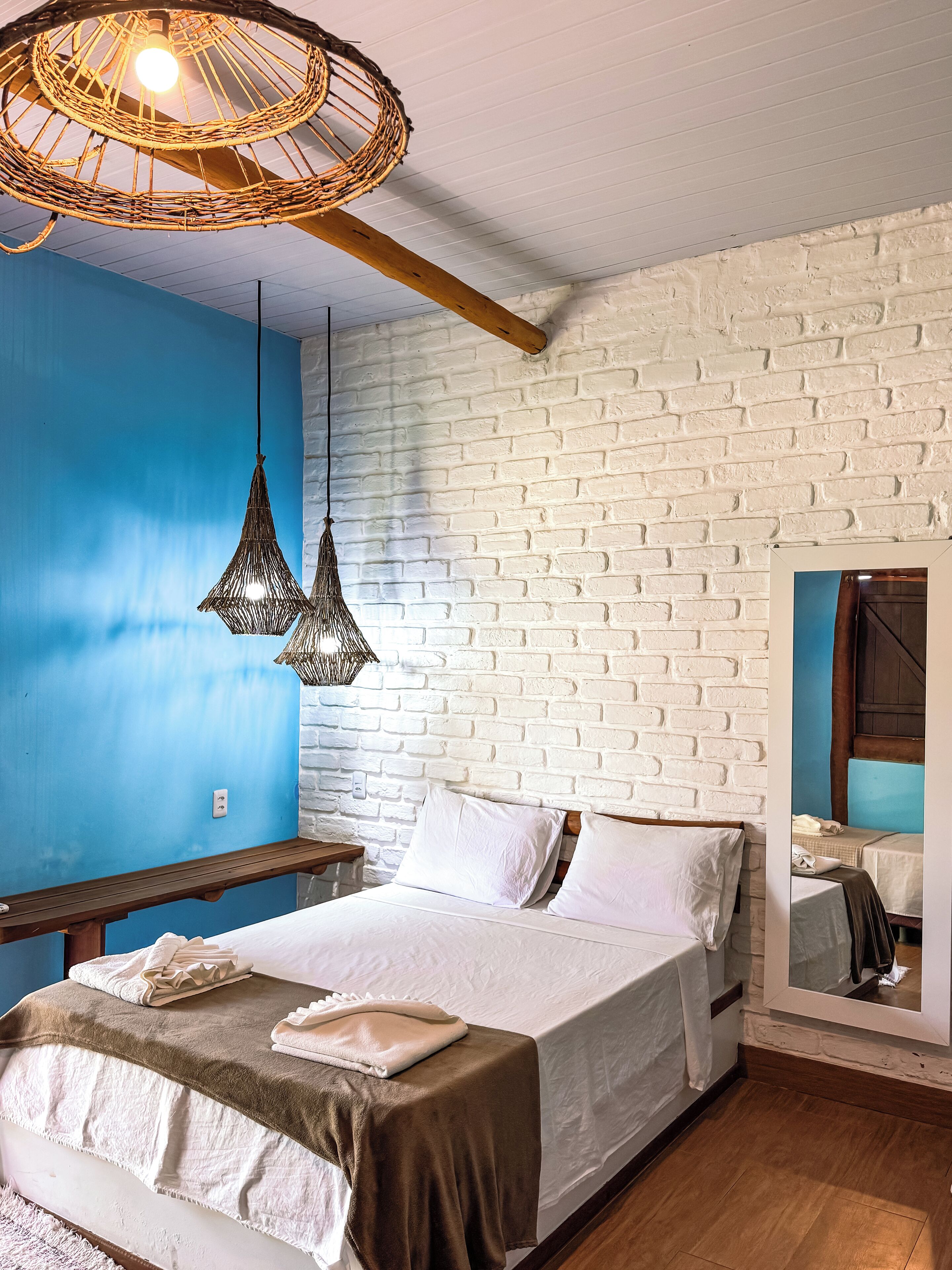 A bedroom with a bed, a wooden bench, a hanging light fixture, and a brick wall.
