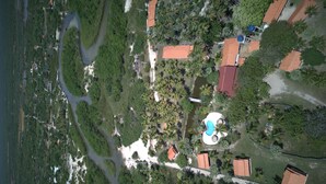 An aerial view of a resort with a swimming pool, palm trees, and a river. - Pousada Rancho do Buna (Barreirinhas)