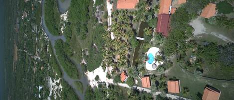 An aerial view of a resort with a swimming pool, palm trees, and a river.