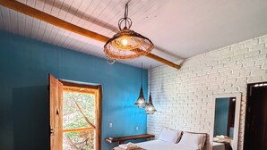 A room with two beds, a large mirror, a hanging light fixture, and a view of greenery through an open door. - Pousada Rancho do Buna (Barreirinhas)