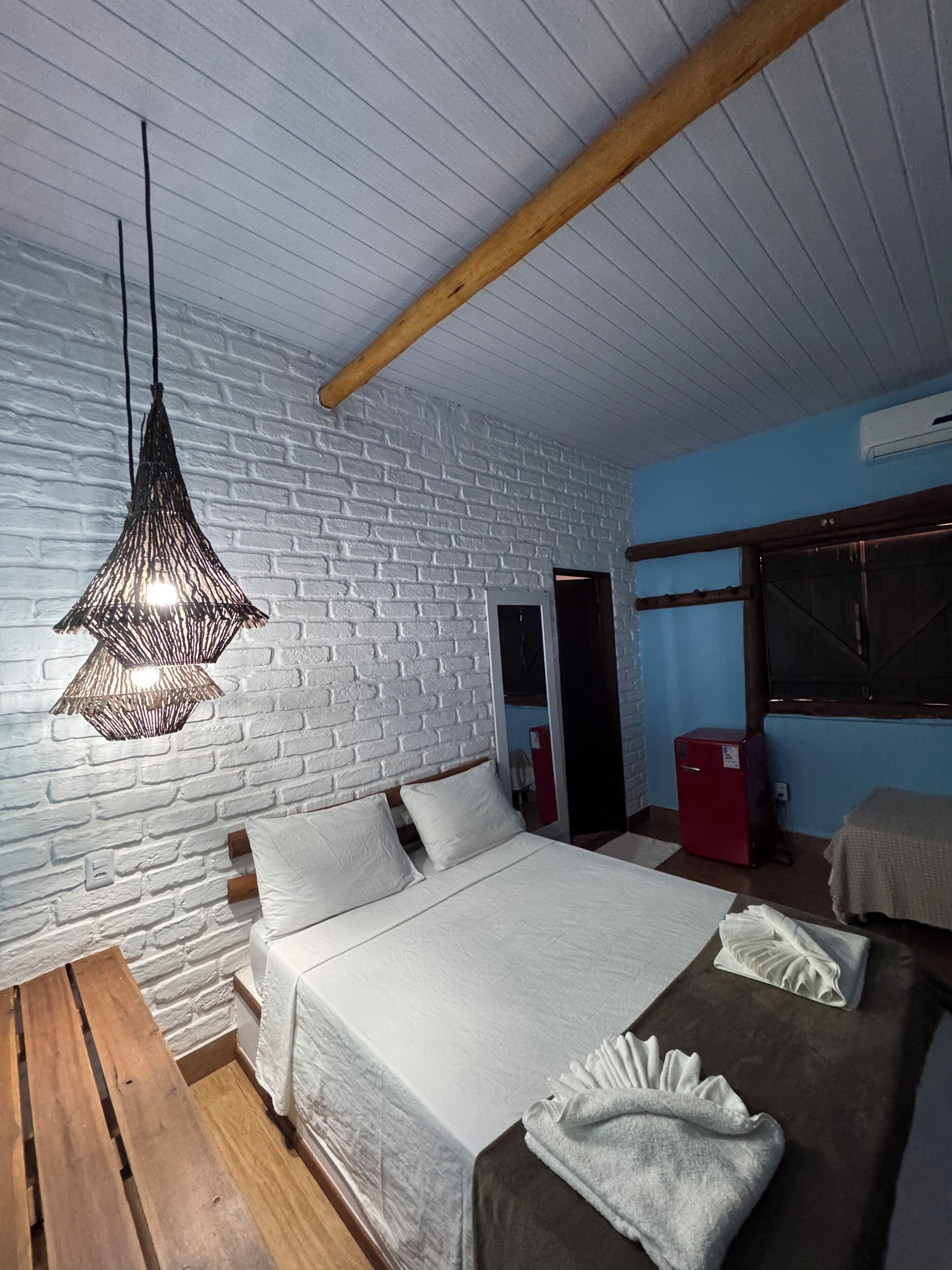 A bedroom with a bed, bedside tables, a hanging light fixture, and a brick wall.