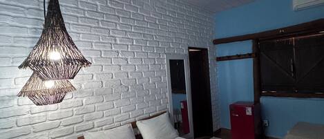 A bedroom with a bed, bedside tables, a hanging light fixture, and a brick wall.