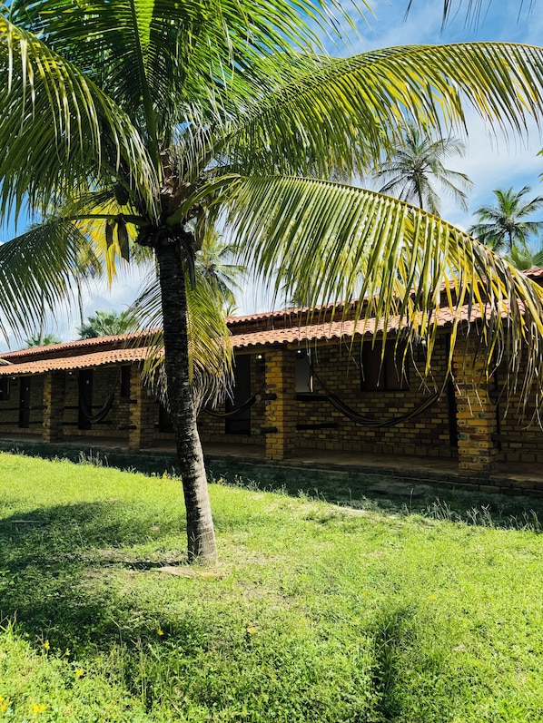 A brick building with a tiled roof and a palm tree in front. - Pousada Rancho do Buna (Barreirinhas)