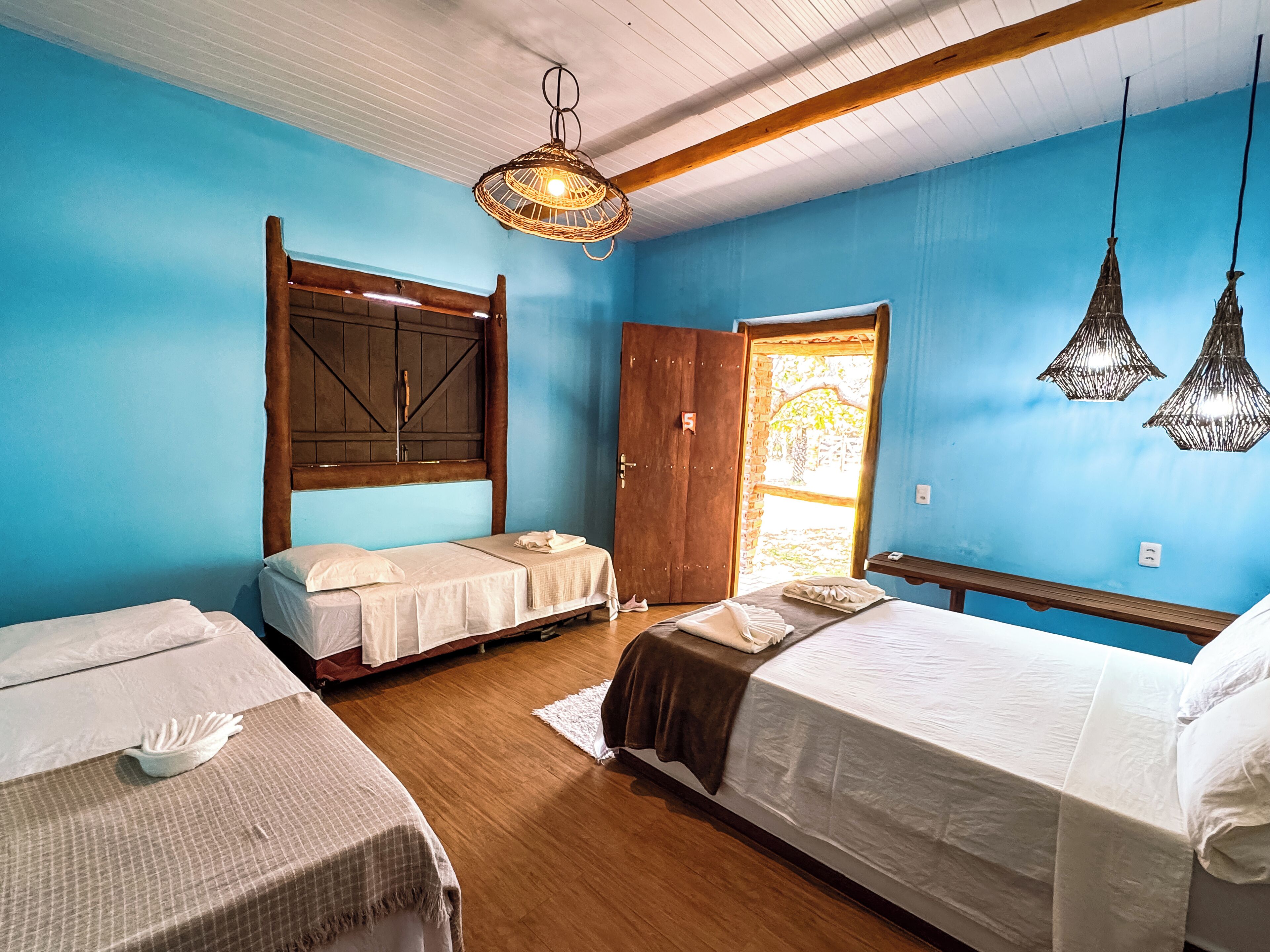 A room with two beds, a wooden headboard, a hanging light fixture, and a door leading to an outdoor area.