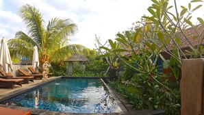A swimming pool with lounge chairs and umbrellas, surrounded by tropical plants and a small gazebo. - The Akah Cottage (Lembongan Island)