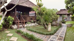 A thatched-roof hut with a wooden staircase leading to a porch, surrounded by lush greenery and a patterned stone pathway. - The Akah Cottage (Lembongan Island)