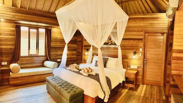 A wooden cabin-style bedroom with a four-poster bed, a bench, and a window with curtains. - The Akah Cottage (Lembongan Island)
