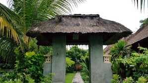 A thatched-roof structure with a stone base, surrounded by lush tropical vegetation. - The Akah Cottage (Lembongan Island)