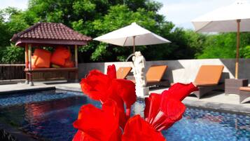 Una piscina con flores rojas al frente, sillas de descanso y sombrillas al fondo.