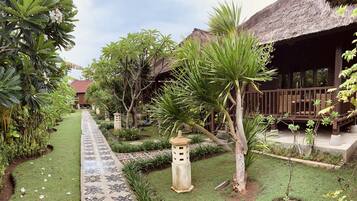 A tropical garden pathway leading to a thatched-roof building with a wooden deck.