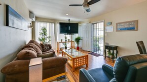 A living room with a sofa, a coffee table, a TV, and a ceiling fan. - Pacific Beach Apartment: Walk to Beach & Pier! (San Diego)
