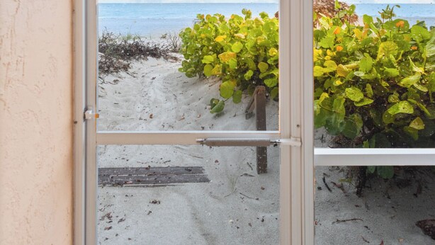 Vista a través de una ventana con una playa y el océano al fondo.
