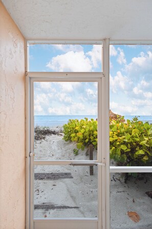 Une vue à travers une fenêtre, avec une plage et l’océan en arrière-plan.