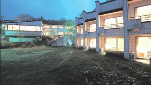Un edificio moderno con varios pisos, grandes ventanales y un área verde al frente.