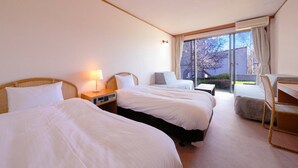 Habitación de hotel con dos camas, un escritorio, una silla y un ventanal con vistas a árboles.