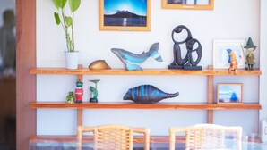 Una habitación con un estante de madera que muestra varios objetos decorativos, una planta en maceta y un cuadro en la pared.