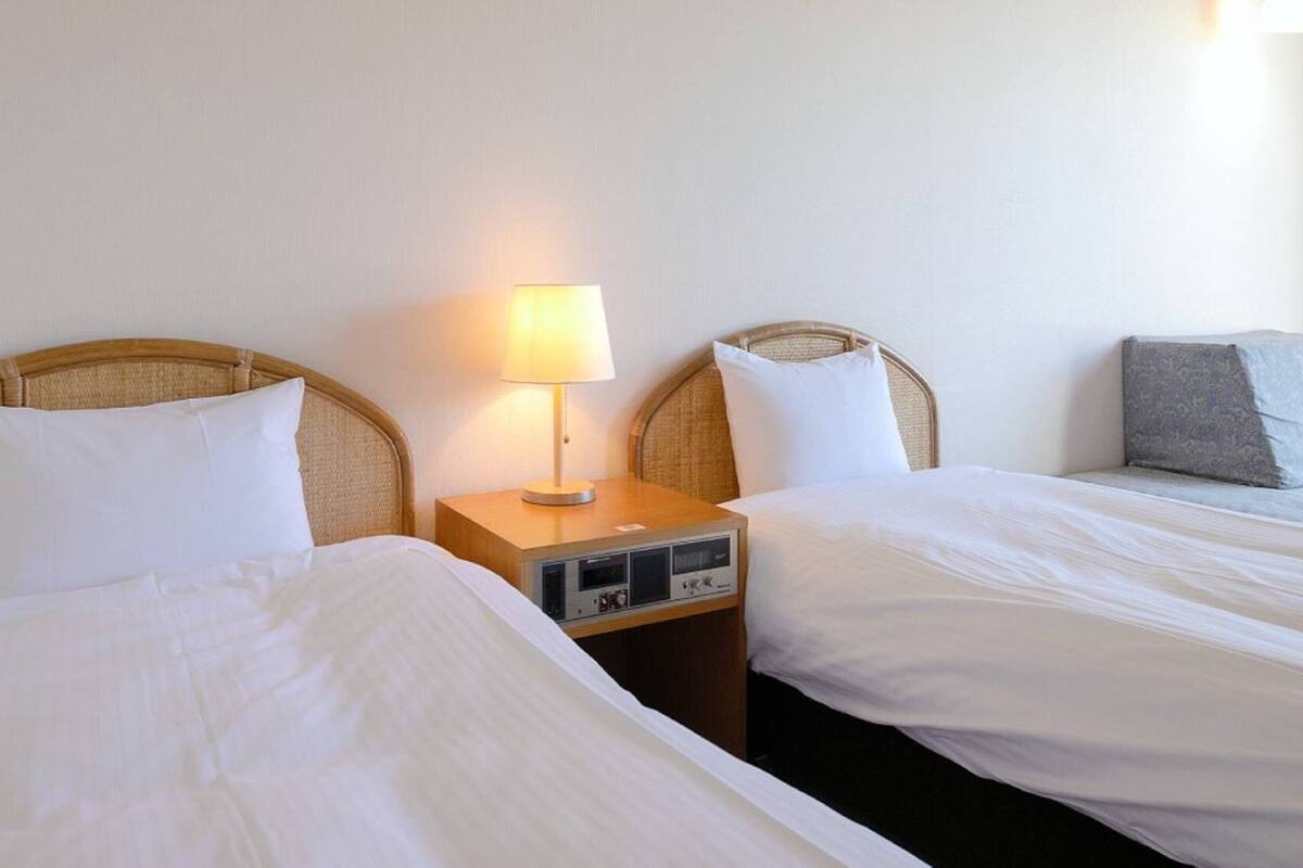 A hotel room with two single beds, a bedside table with a lamp, and a nightstand with a radio.