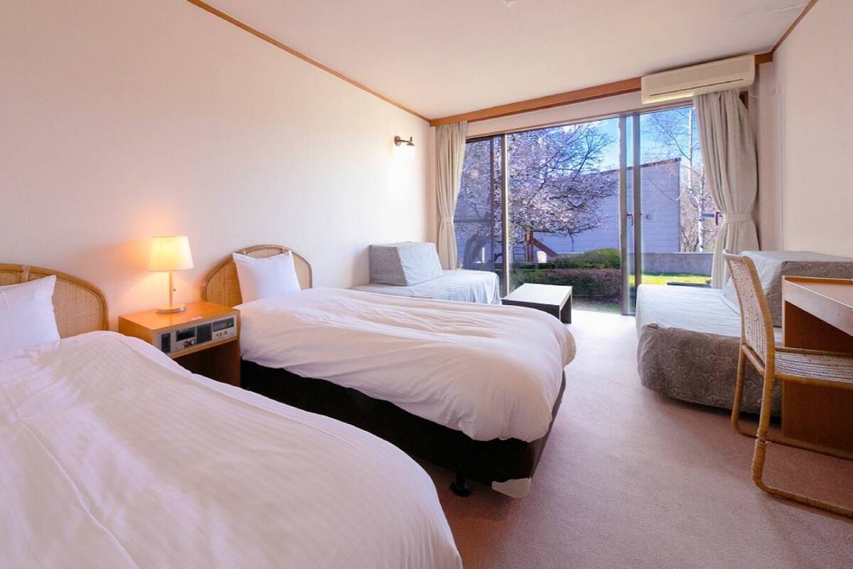 A hotel room with two beds, a desk, a chair, and a view of the outdoors.