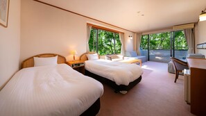 Habitación de hotel con dos camas, un escritorio y un balcón con vista a árboles.