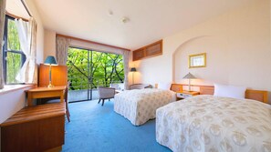 Habitación de hotel con dos camas, un escritorio, una silla y ventana con vista a árboles.