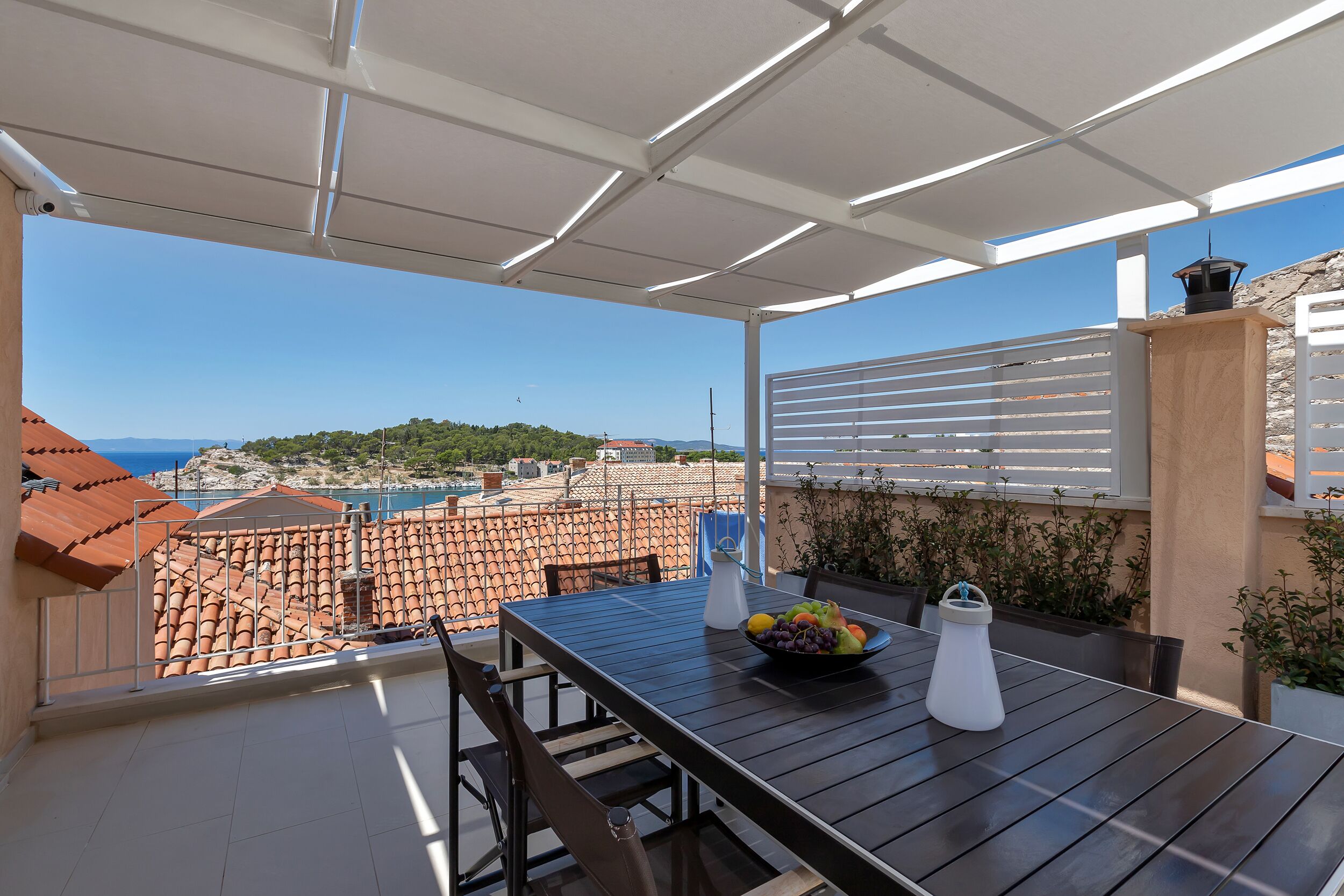 A balcony with a table, chairs, a bowl of fruit, and a water bottle.