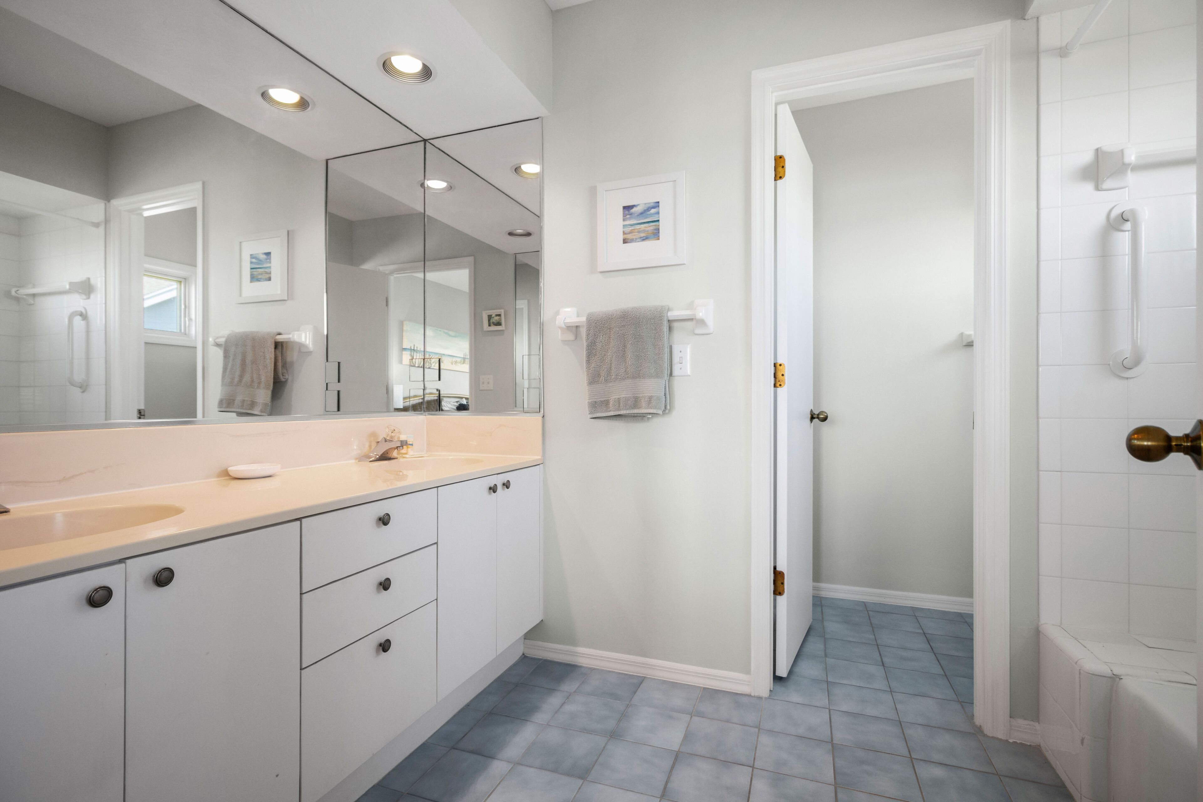 A modern bathroom with a large mirror, white cabinets, a beige countertop, and a blue-tiled floor.