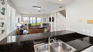 A modern kitchen with a black granite countertop, stainless steel sink, and a ceiling fan. - Cedars East Bayview Tennis & Pool Unit 822 by RVA (Longboat Key)