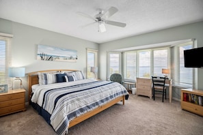A bedroom with a bed, desk, chair, and a ceiling fan.