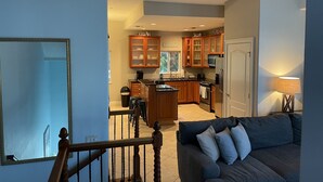 A modern kitchen with wooden cabinets, a central island, and a dining area with a dark-colored sofa.
