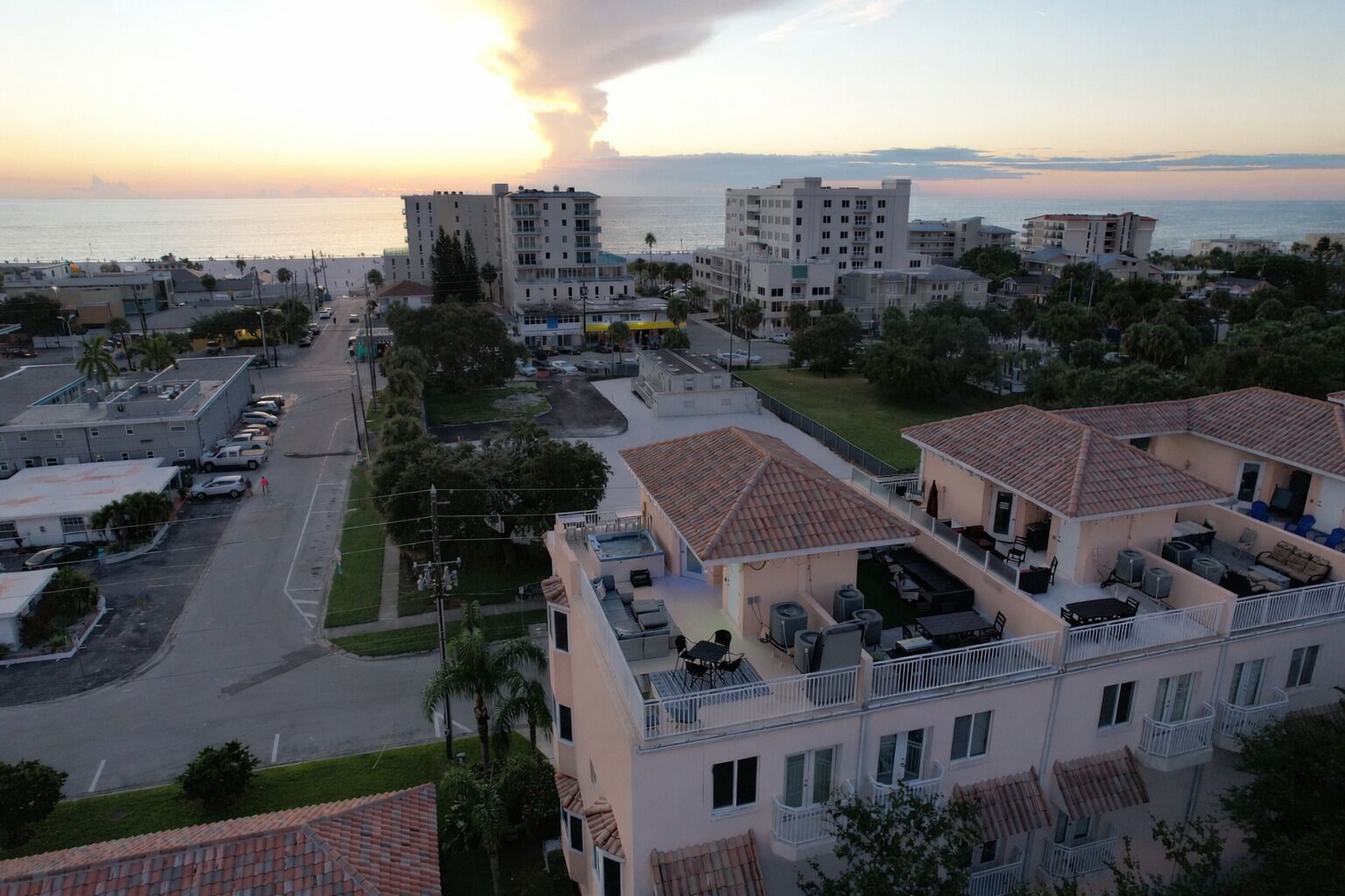 Zona residencial costera con edificios de varios pisos, una calle y vista al mar al atardecer.